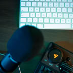 A sleek podcasting setup featuring a microphone, audio control panel, and keyboard.