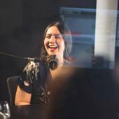 A woman smiles while recording a podcast indoors with a microphone.